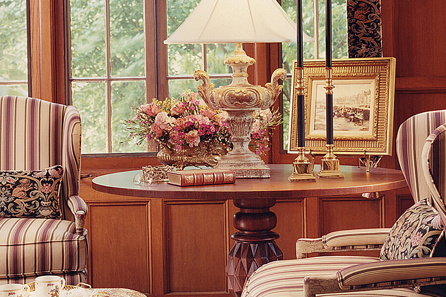 a round wood table topped with a lampshade, a picture and books surrounded by two chairs.